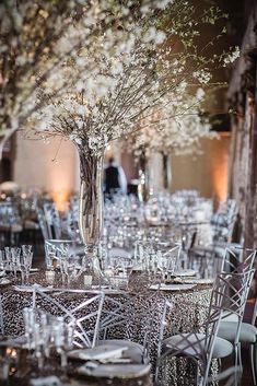 the tables are set with clear chairs and white flowers in vases on each table