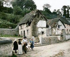 an old photo of people standing in front of a house with thatched roof and stone walls