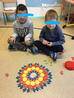 two young boys sitting on the floor playing with colored shapes and paper circles in front of them