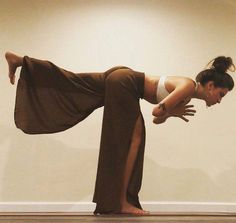 a woman in brown pants and white shirt doing a yoga pose with her legs spread out