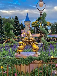 two golden statues in the middle of a garden with trees and flowers around them,