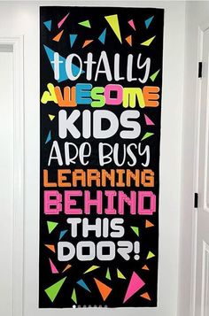 a black and white wall hanging on the side of a door with colorful lettering that says, totally awesome kids are busy learning behind this door