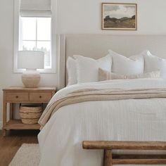 a bed with white linens and pillows in a bedroom next to a wooden table