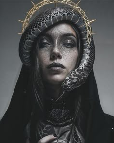 a woman in black and white makeup with a snake wrapped around her head, wearing a crown