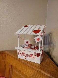 a small white box with hearts on it sitting on top of a wooden dresser next to a wall