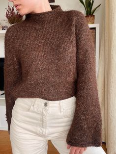 a woman wearing a brown sweater and white pants