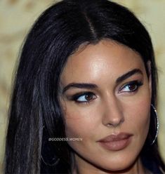 a close up of a woman with long hair and blue eyeshadow wearing large hoop earrings