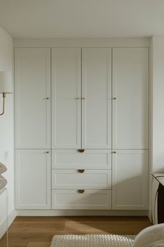 a white closet with gold handles and drawers in a room that has wood flooring