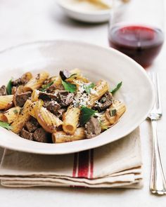 a white bowl filled with pasta and meat covered in parmesan cheese next to a glass of red wine