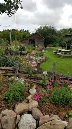 a garden with rocks and flowers in the foreground, next to a picnic table