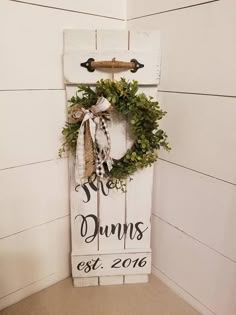 a wooden sign with a wreath hanging on it's side in front of a white wall