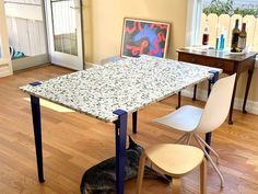 a dog sitting under a table in a room with hardwood floors and yellow walls, next to a white chair