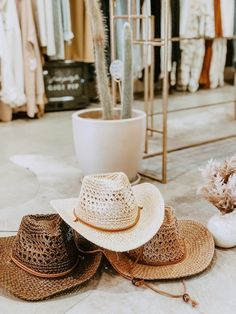 three straw hats sitting on the ground in front of a rack with clothes and other items