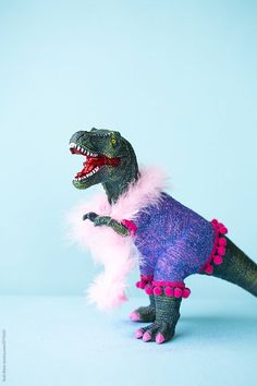 a toy dinosaur with pink and purple feathers on it's back, standing in front of a blue background