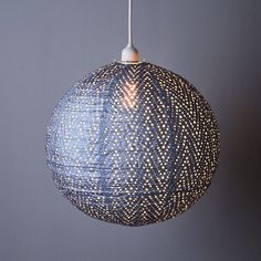 a blue and white lamp hanging from a gray wall with a light bulb in the middle