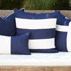 three blue and white pillows sitting on top of a wooden bench next to palm trees