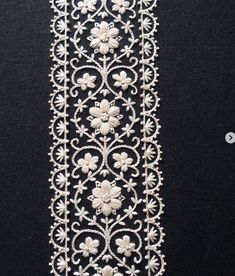 a white beaded ribbon with flowers and leaves on the side, attached to a black background