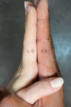 two hands holding each other with the word love tattooed on their thumbnails in front of them