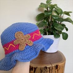 a crocheted blue hat with a teddy bear on it next to a potted plant