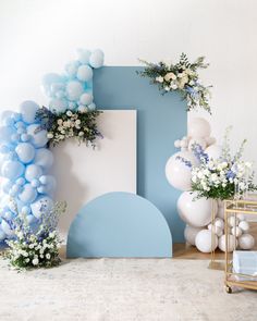 blue and white balloons are on display in front of an arch with flowers, greenery and other decorations