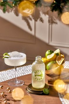 a bottle of lemonade next to a glass filled with ice and limes on a table