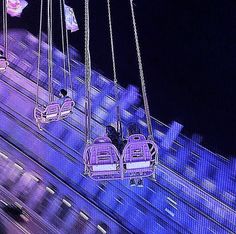 some people are riding on swings in the air at an amusement park with lights and buildings behind them