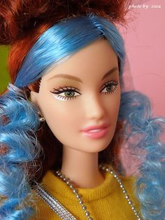 a close up of a doll with blue hair and pearls on her head, wearing a yellow sweater