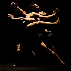 two dancers are performing in the dark with their arms extended and legs spread out,