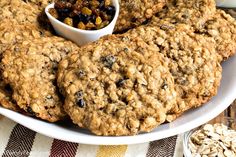 a white plate topped with oatmeal cookies next to a bowl of raisins