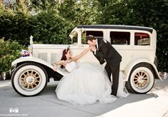 a bride and groom posing in front of an antique car