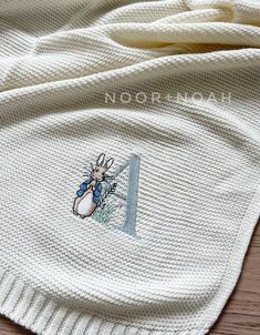 a white knitted blanket with a cartoon rabbit on it's chest and the letter n