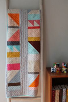 a multicolored quilt hanging on the wall next to a book shelf with books