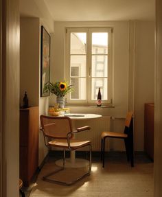 an empty room with a chair, table and vase on the window sill in it