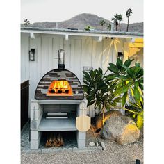 an outdoor pizza oven in front of a white house with palm trees and rocks around it