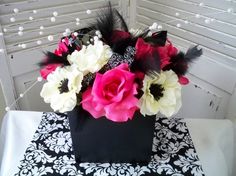 a black and white table cloth with pink, white and red flowers in a square vase