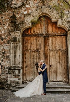 a bride and groom kissing in front of an old door at their wedding venue,