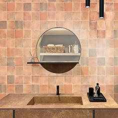 a bathroom sink sitting under a round mirror next to a shelf with bottles and cups on it