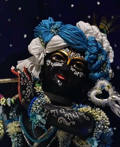 a black mask with blue hair and flowers on it's head is surrounded by beads