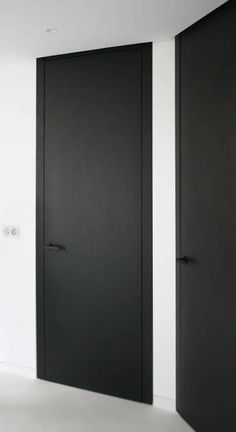 an empty room with two black doors and white walls in the center, there are no people