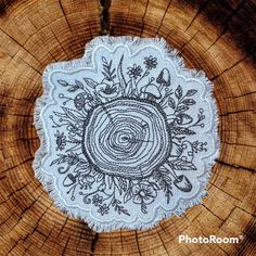 a white doily with black embroidery on top of a tree stump in the woods