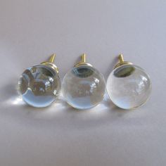 three glass knobs with gold colored handles on a white surface, set against a plain background