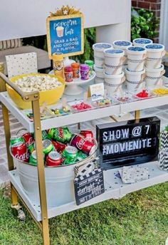 an outdoor movie party with popcorn buckets and movies on the table, signs in front of it