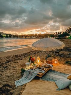 a table set up on the beach with an umbrella over it and candles in front of it