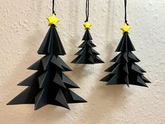 three black paper christmas trees hanging from strings with yellow stars on each ornament