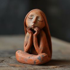 a small clay figurine sitting on top of a wooden table with its eyes closed