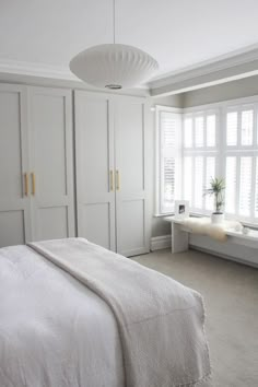 a bedroom with white furniture and large windows in it's center wall, along with a bed on the other side