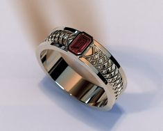 a close up of a ring on a white surface with a red stone in the center