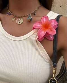 a woman wearing a white tank top holding a pink flower in her right hand and a black leather belt around her neck