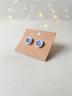 a pair of blue and white earrings sitting on top of a cardboard box with string lights in the background