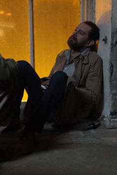 a man sitting on the ground next to a window with yellow light coming through it